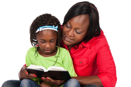 Adorable small african child with braids wearing a bright green shirt and blue jeans and her mother wearing a red shirt. The mom is reading to the girl from a book.の写真素材