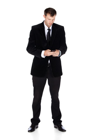 Handsome young successful caucasian businessman wearing a formal black suit, tie and white shirt. The man is typing on and looking at his mobile phone.の写真素材
