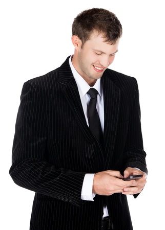 Handsome young successful caucasian businessman wearing a formal black suit, tie and white shirt. The man is typing on and looking at his mobile phone and is smiling.の写真素材