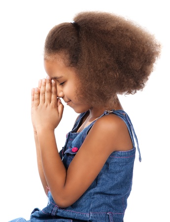 Adorable cute african child with afro hair wearing a denim dress. The girl is kneeling and praying.の写真素材