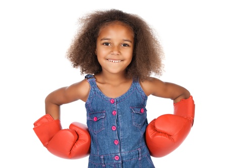 Adorable cute african child with afro hair wearing a denim dress. The girl is wearing big red boxing gloves.の写真素材