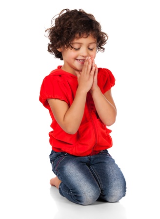 Adorable small caucasian child with curly hair wearing a bright red hooded top and blue jeans. The girl is kneeling and praying.の写真素材