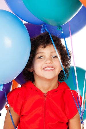 Adorable small caucasian child with curly hair wearing a bright red hooded top. The girl is holding a bunch of bright coloured helium balloons.の写真素材