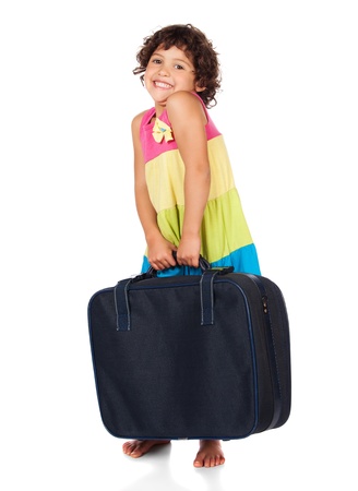 Adorable small caucasian child with curly hair wearing a pink blue and yellow dress. The girl is holding a dark blue suitcase.の写真素材