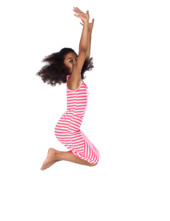Adorable cute african child with afro hair wearing a white and pink striped dress. The girl is jumping and smiling.の写真素材