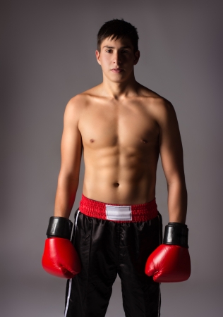 Young handsome male caucasian kickboxer wearing red boxing gloves and kickboxing gear isolated on a neutral backgroundの写真素材