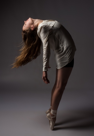 Beautiful slim young female modern jazz contemporary style ballet dancer on pointe shoes wearing a black leotard and white shirt on a neutral grey studio backgroundの写真素材