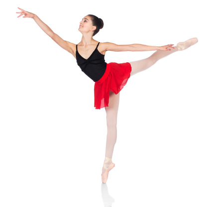 Beautiful female ballet dancer isolated on a white background. Ballerina is wearing a black leotard, pink stockings, pointe shoes and a red dress.の写真素材