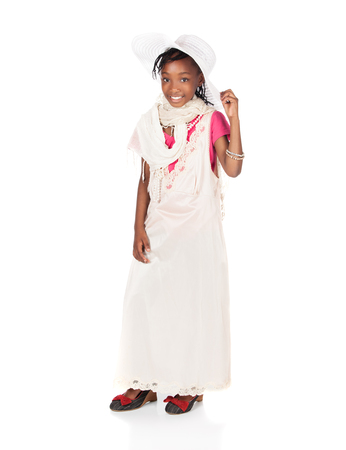 Pretty cute african girl is playing dress up. She is wearing a beige dress, white hat and hight heel shoes.の写真素材