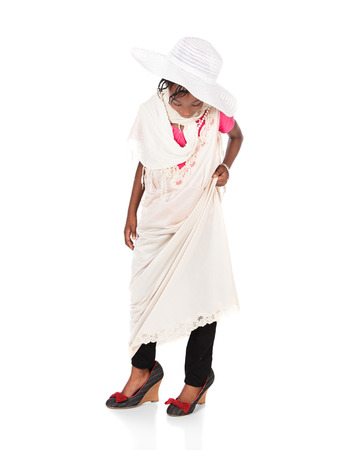 Pretty cute african girl is playing dress up. She is wearing a beige dress, white hat and hight heel shoes.の写真素材
