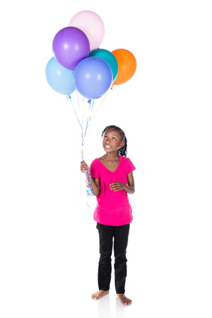 Adorable small african child with braids wearing a bright green shirt and black skinny jeans. The girl is holding a bunch of bright coloured helium balloons.の写真素材