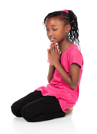 Adorable small african child with braids wearing a bright green shirt and black skinny jeans. The girl is kneeling and praying.の写真素材