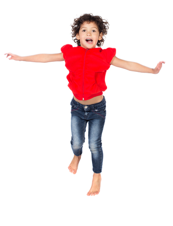Adorable small caucasian child with curly hair wearing a bright red hooded top and blue jeans. The girl is jumping and smiling.の写真素材