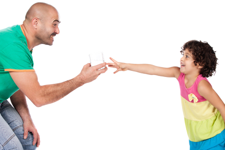 Adorable small caucasian child with curly hair wearing a pink blue and yellow dress is reaching for a glass of water in the hand of her father.の写真素材