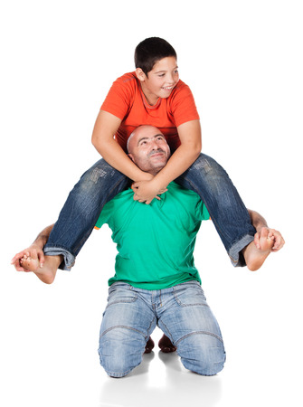 Young caucasian boy wearing an orange t-shirt and blue jeans is playing with his father. The dad is wearing a green shirt. The boy is on the father's shoulders.の写真素材