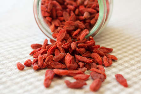 Healthy red natural dried goji berries in a upset glass jar on a checkered table clothの写真素材