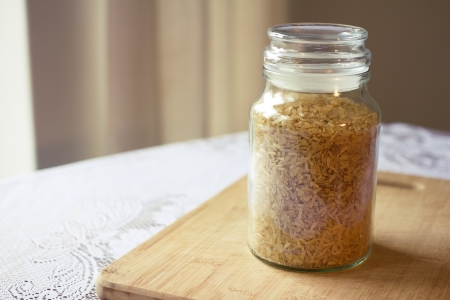 Glass jar with uncooked brown rice on a wooden chopping board. Image contains copy space.の写真素材