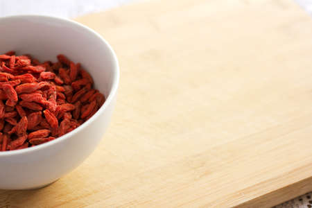 Healthy red natural dried goji berries in a in a white bowl on a wooden chopping board. Image contains copy space.の写真素材