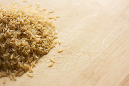 Heap of uncooked brown rice on a wooden chopping board. Image contains copy space.の写真素材