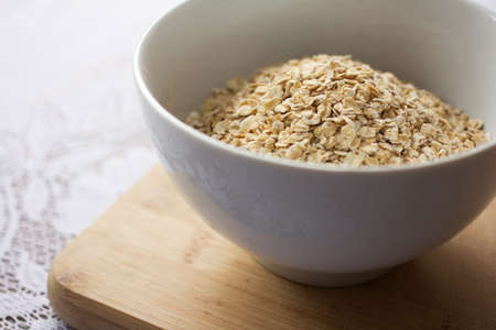 White bowl with uncooked oats on a wooden chopping board.の写真素材