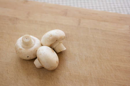 White button mushrooms on a wooden chopping board. Image contains copy space.の写真素材