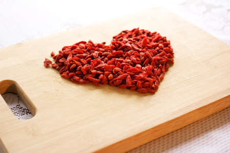 Pile of healthy red natural dried goji berries on a wooden chopping board arranged in the shape of a heart.の写真素材