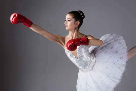Beautiful female ballet dancer on a grey background. Ballerina is wearing a white tutu, pointe shoes and red boxing gloves.の写真素材