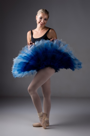 Beautiful female ballet dancer on a grey background. Ballerina is wearing a black leotard; pink stockings; pointe shoes and a blue tutu.の写真素材