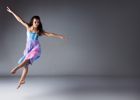 Beautiful female modern jazz contemporary style dancer on a grey background. Dancer is barefoot and wearing a blue and purple dress.の写真素材