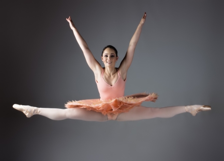Beautiful female ballet dancer on a grey background. Ballerina is wearing an orange tutu, pink stockings and pointe shoes.の写真素材