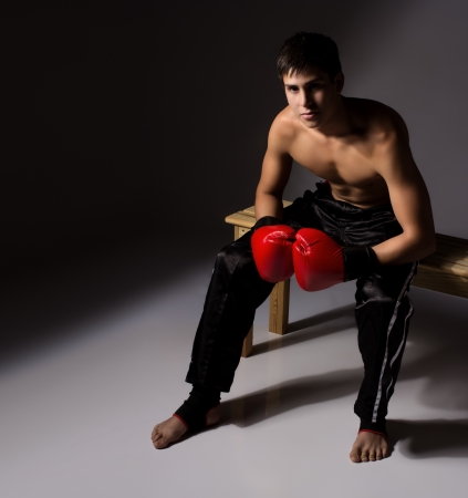 Young handsome male caucasian kickboxer wearing red boxing gloves and kickboxing gear isolated on a neutral backgroundの写真素材