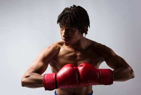 Young muscular athletic male boxer wearing blue boxing shorts and red boxing gloves. Fighter is on a grey background.の写真素材