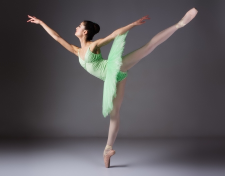 Beautiful female ballet dancer on a grey background. Ballerina is wearing a green tutu and pointe shoes.の写真素材