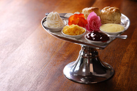 Delicious butter scones on a silver heart shaped tray served with roses cheese cream and jam preserves on a wooden table.の写真素材