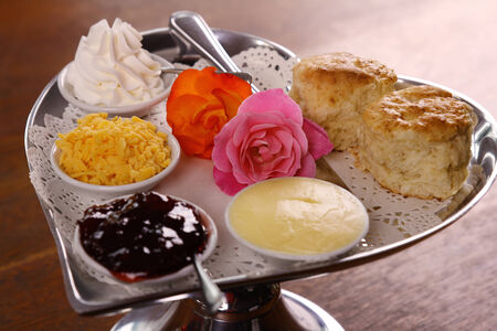 Delicious butter scones on a silver heart shaped tray served with roses cheese cream and jam preserves on a wooden table.の写真素材