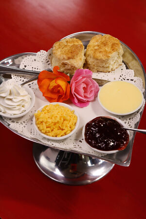 Delicious butter scones on a silver heart shaped tray served with roses cheese cream and jam preserves on a red wooden table.の写真素材