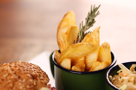 Delicious chicken burger with chopped salad served with potato wedges on a white plate on a wooden table.の写真素材