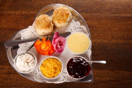 Delicious butter scones on a silver heart shaped tray served with roses cheese cream and jam preserves on a wooden table. Image contains copy space.の写真素材