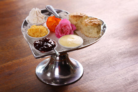 Delicious butter scones on a silver heart shaped tray served with roses cheese cream and jam preserves on a wooden table.の写真素材