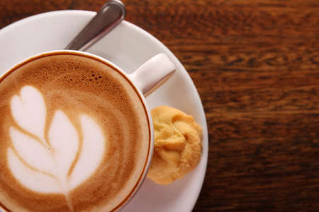 Delicious aromatic cappuccino in a white porcelain cup with a biscuit on the side on a wooden table. Image contains copy space.の写真素材