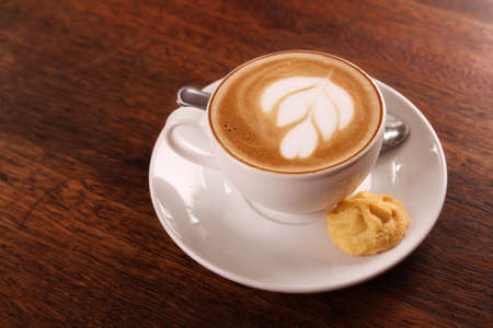Delicious aromatic cappuccino in a white porcelain cup with a biscuit on the side on a wooden table. Image contains copy space.の写真素材