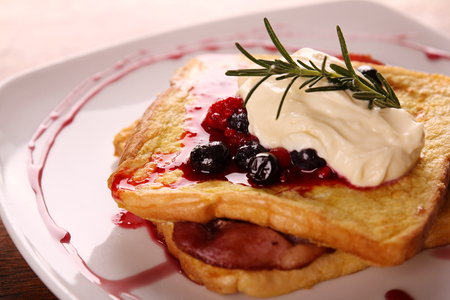 Delicious french toast with bacon syrup berries and cream on a white plate on a wooden table.の写真素材