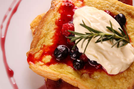 Delicious french toast with bacon syrup berries and cream on a white plate on a wooden table.の写真素材