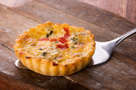 One savory quiche served on a wooden board with a silver cake lifter.の写真素材