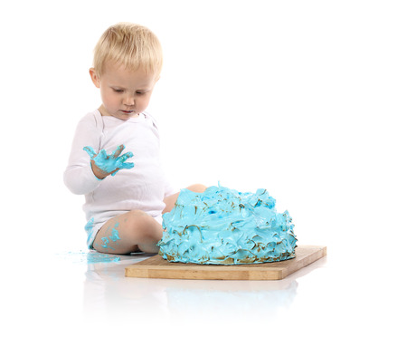 A one year old baby boy smashing a blue iced birthday cake on a wooden board. Image is isolated on a white background.の写真素材