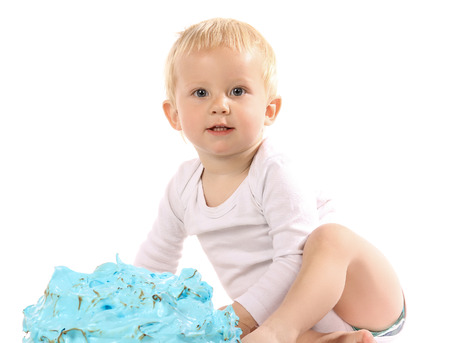 A one year old baby boy smashing a blue iced birthday cake on a wooden board. Image is isolated on a white background.の写真素材