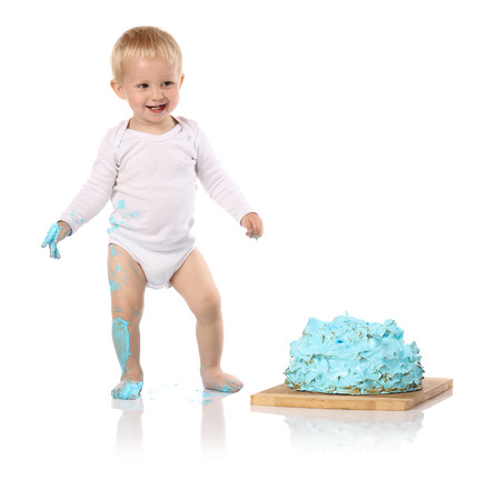 A one year old baby boy smashing a blue iced birthday cake on a wooden board. Image is isolated on a white background.の写真素材