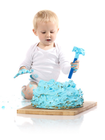 A one year old baby boy smashing a blue iced birthday cake with a toy hammer on a wooden board. Image is isolated on a white background.の写真素材