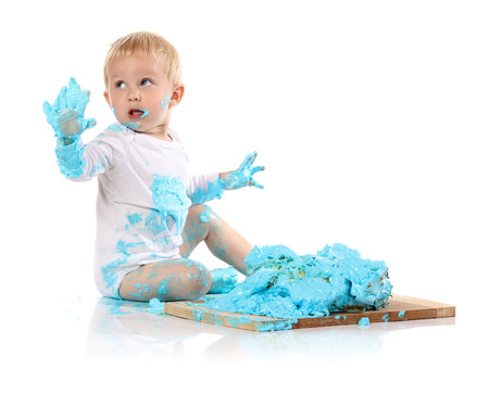 A one year old baby boy smashing a blue iced birthday cake on a wooden board. Image is isolated on a white background.の写真素材