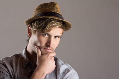 Portrait of a handsome blonde caucasian man wearing a faded blue button shirt with an olive beige straw hat.の写真素材